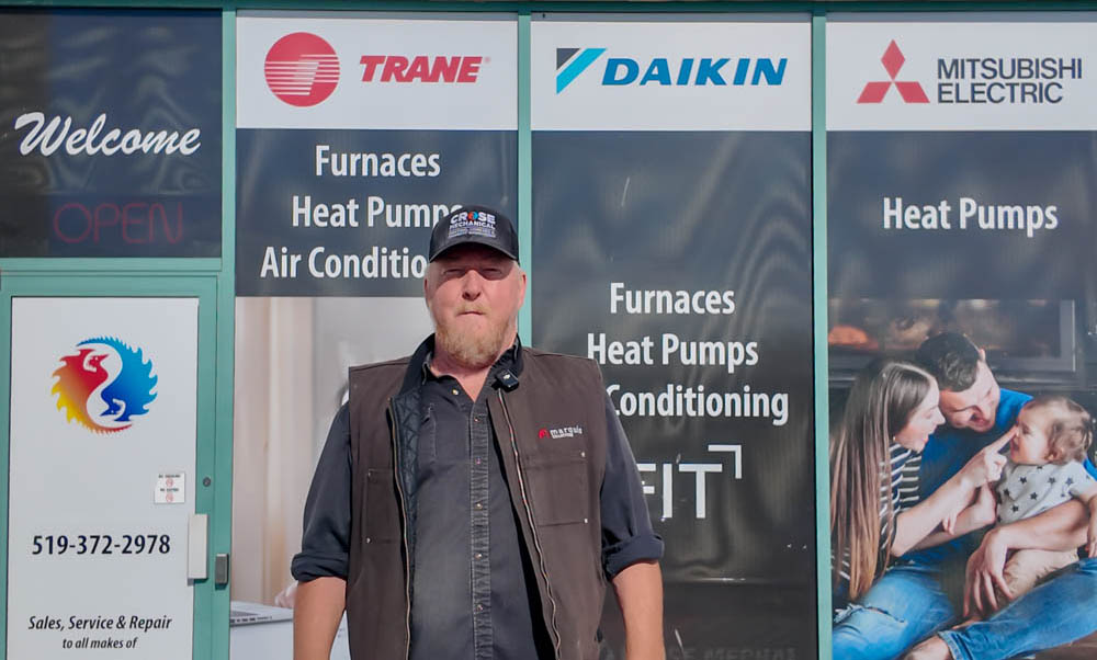 A heating and cooling contractor outside his shop, with furnace and heat pump signs in the window